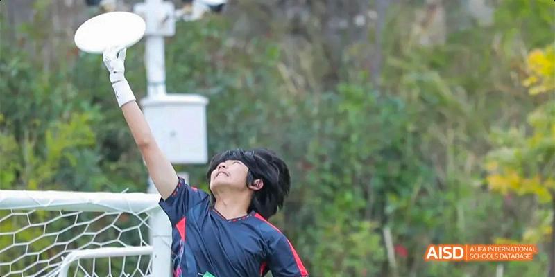 A male student in a dark shirt looking up with a concentrated expression while participating in an outdoor sports event, at Beanstalk International Bilingual School.
