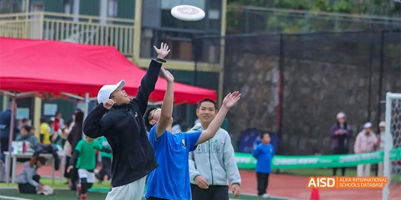 Students playing an outdoor game with a flying disc or frisbee, with one student reaching high to catch it, at Beanstalk International Bilingual School.