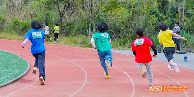 A student in a bright teal shirt running away from the camera on a red outdoor track during an athletic event, at Beanstalk International Bilingual School.