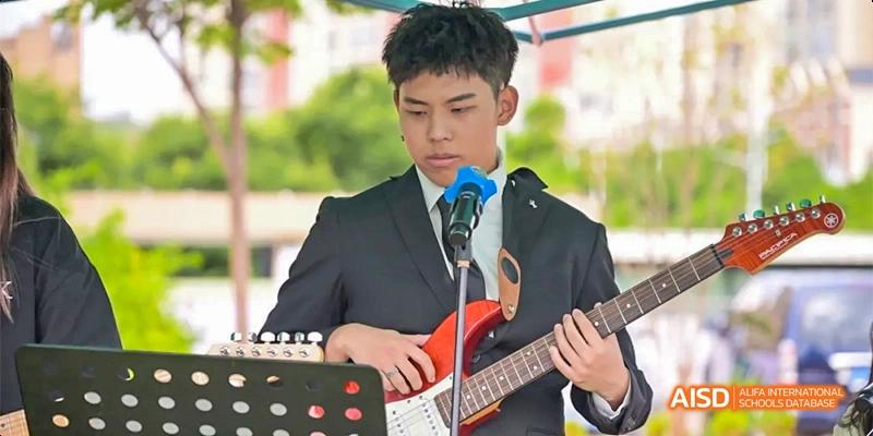 A young man in a suit playing an electric guitar and singing into a microphone during a performance, at Beanstalk International Bilingual School.