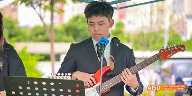 A young man in a suit playing an electric guitar and singing into a microphone during a performance, at Beanstalk International Bilingual School.