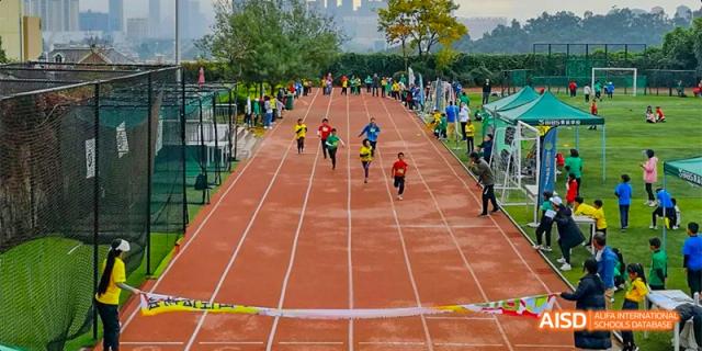 Multiple students running a sprint race on a brown outdoor track, viewed from a high angle, at Beanstalk International Bilingual School.