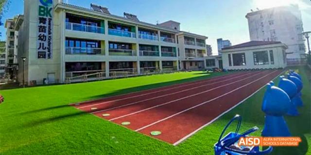 An exterior shot of a large, modern school building with multiple windows, next to a well-maintained red track and a green turf field, at Beanstalk International Bilingual School.