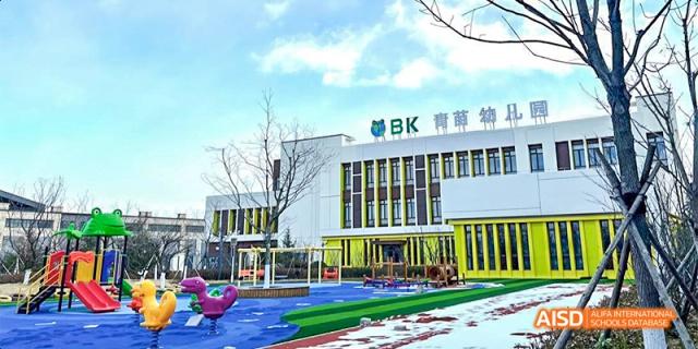 An exterior view of a modern school building with a blue and white facade and a colorful playground area in front, at Beanstalk International Bilingual School.