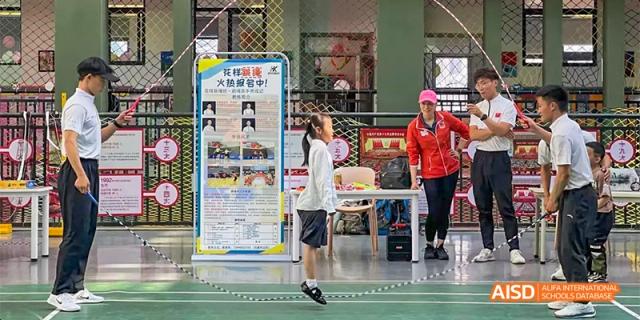 A student jumping or reaching for a high point indoors, with posters and a sports instructor visible in the background, at Beanstalk International Bilingual School.