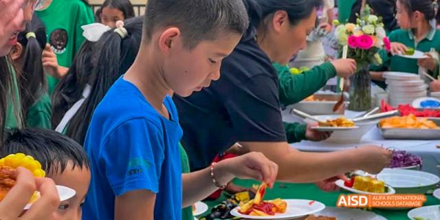 A male student in a blue shirt picking up food from a serving tray during a meal or catering event, at Beanstalk International Bilingual School.