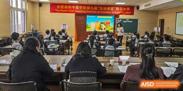 A teacher presents to a large classroom of students during a teaching seminar. Behind the students, observers watch from the back at Hefei High-tech Sino-Canadian School.