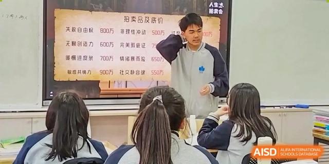 A student stands at the front of a classroom presenting to his peers next to a digital display showing a points-based activity at Hefei High-tech Sino-Canadian School.