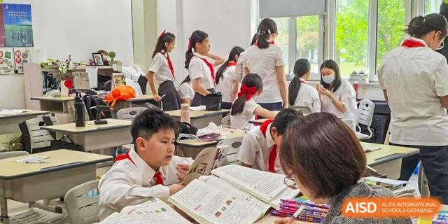 Young students in school uniforms work collaboratively at their desks, focusing on textbooks and shared assignments at Hefei High-tech Sino-Canadian School.