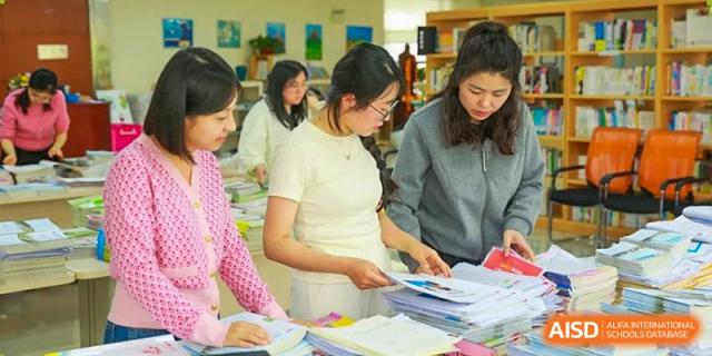 Four female educators or staff members work together to organize and sort through large stacks of papers and books at Hefei High-tech Sino-Canadian School.