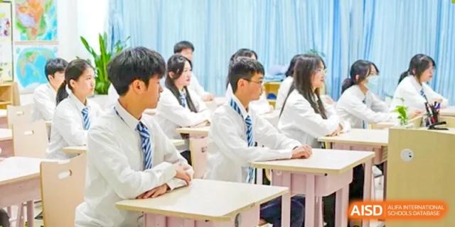 High school students in white shirts and blue ties sit attentively at their desks during a lecture in a bright classroom at Hefei High-tech Sino-Canadian School.