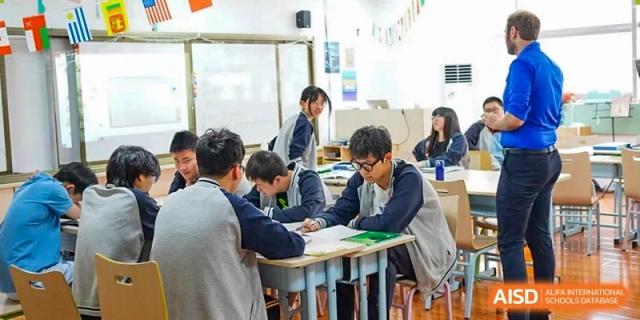 Students collaborate in small groups, working together on a classroom assignment while seated at their desks at Hefei High-tech Sino-Canadian School.