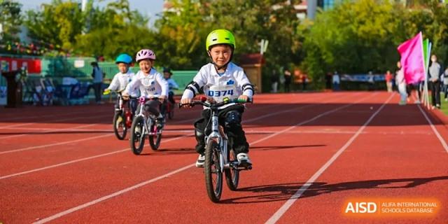 Young students wearing safety helmets and gear enjoy a group cycling activity on the outdoor running track at Hefei High-tech Sino-Canadian School.