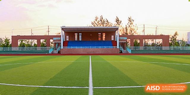 A wide-angle view of the green synthetic turf field and the grandstand seating at the outdoor sports complex of Hefei High-tech Sino-Canadian School.