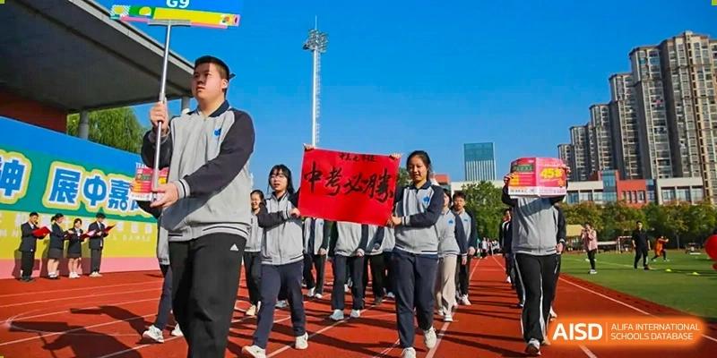 A group of students proudly march across the track field holding a large red banner during a school event at Hefei High-tech Sino-Canadian School.