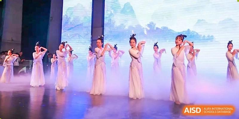 Students in traditional white gowns perform a graceful dance on a stage with blue atmospheric lighting at Hefei High-tech Sino-Canadian School.