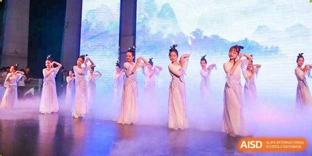 Students in traditional white gowns perform a graceful dance on a stage with blue atmospheric lighting at Hefei High-tech Sino-Canadian School.