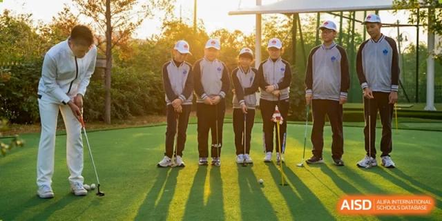 Four students in matching uniforms practice their golf swings together on a sunny outdoor putting green at Hefei High-tech Sino-Canadian School.