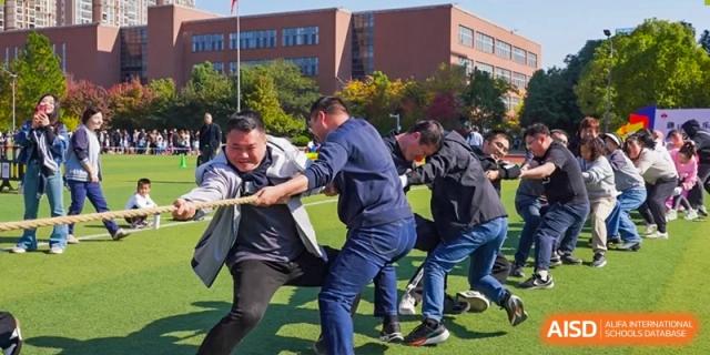 A group of men engages in a spirited and competitive tug-of-war match on the grass during a field day at Hefei High-tech Sino-Canadian School.