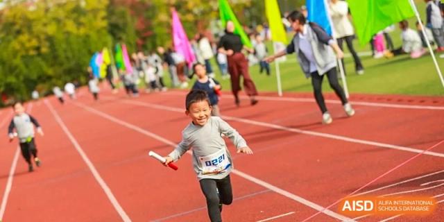 A young boy smiles joyfully while running with a relay baton during a track and field event at Hefei High-tech Sino-Canadian School.