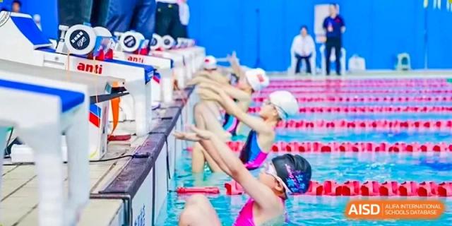 Young swimmers in pink caps and goggles prepare to dive into the water for a race at the indoor pool of Hefei High-tech Sino-Canadian School.