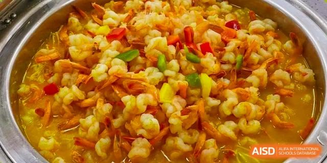 A close-up shot shows a freshly prepared dish of shrimp stir-fried with colorful peppers and vegetables at Hefei High-tech Sino-Canadian School.