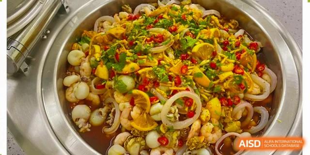 A large serving bowl is filled with a vibrant seafood salad featuring shrimp, lemon slices, and fresh herbs at Hefei High-tech Sino-Canadian School.