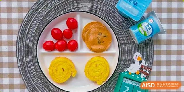 A child's partitioned plate holds a balanced meal of cherry tomatoes, small pancakes, and egg rolls at Hefei High-tech Sino-Canadian School.