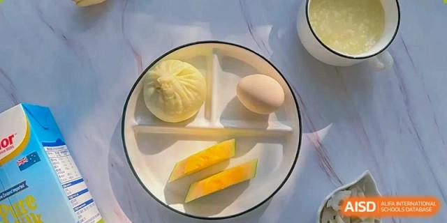 A minimalist breakfast presentation on a white plate includes a steamed bun, a boiled egg, and sliced fruit at Hefei High-tech Sino-Canadian School.