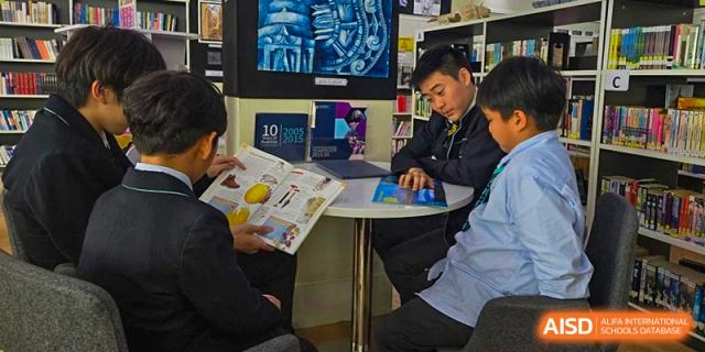 A student from The British School of Guangzhou sitting in the library or study area, focused on a magazine or printed material.