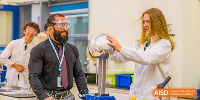 A student or teacher at The British School of Guangzhou demonstrating a high-voltage static electricity experiment using a Van de Graaff generator.