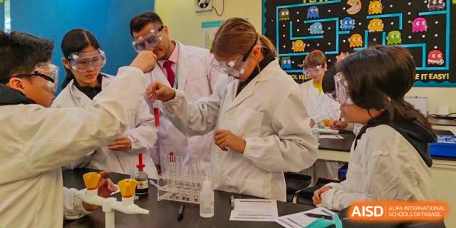 A teacher or staff member at The British School of Guangzhou in a lab coat and safety goggles, carefully handling beakers in a science lab.