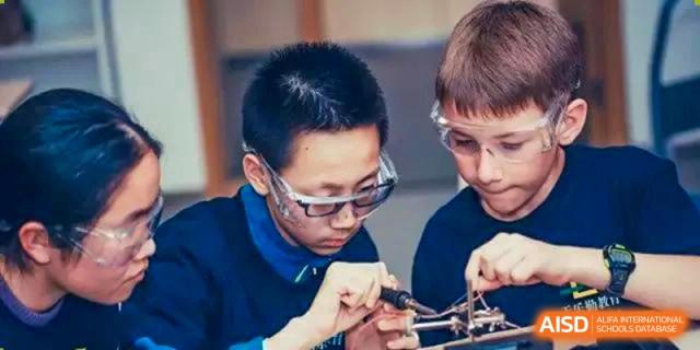 Two male students from The British School of Guangzhou wearing safety goggles and working intently on a robotics or electronics project.
