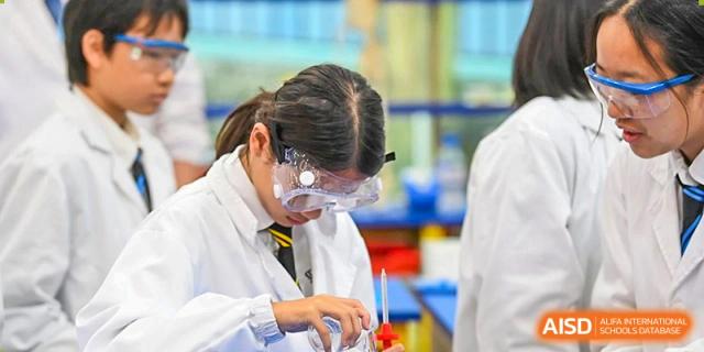 A female student from The British School of Guangzhou wearing a lab coat and safety goggles, conducting a science experiment.