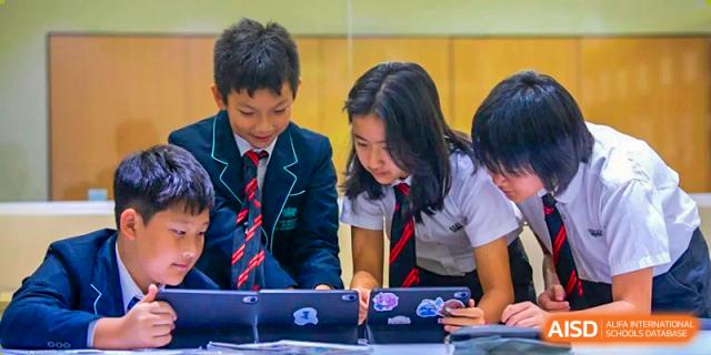 Students from The British School of Guangzhou in uniform collaborating on a task using digital tablets at a desk.