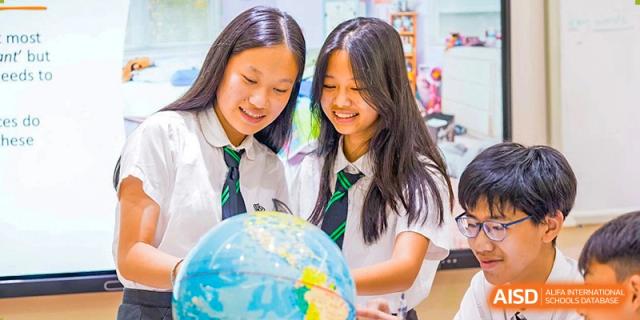 Two female students from The British School of Guangzhou smiling while examining a globe or working on a geography project.