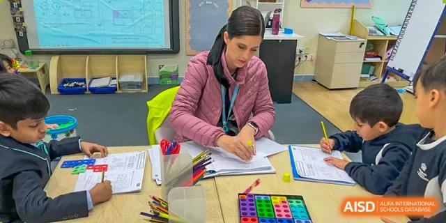 An adult at The British School of Guangzhou is focused on writing or marking papers, surrounded by colored pencils and art supplies.