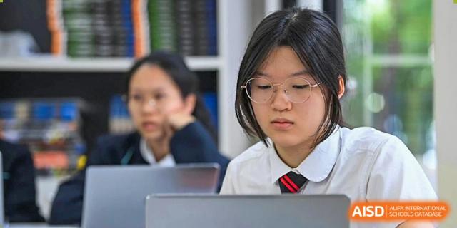 A female student from The British School of Guangzhou wearing glasses and concentrating on her work on a laptop in the classroom.