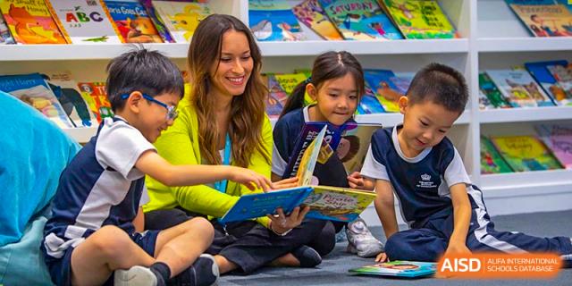 A teacher at The British School of Guangzhou sitting on the floor, reading an engaging story book aloud to a group of young students.