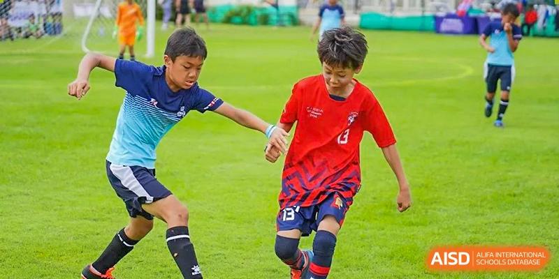 Two young students from The British School of Guangzhou playing football (soccer) intensely on a green field during a match.