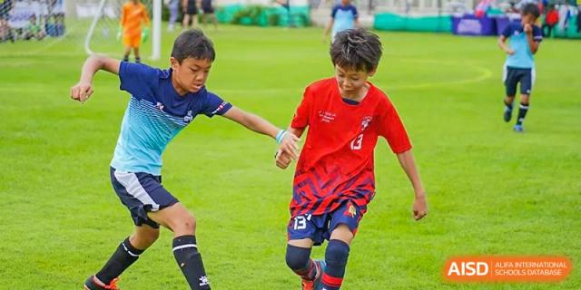 Two young students from The British School of Guangzhou playing football (soccer) intensely on a green field during a match.