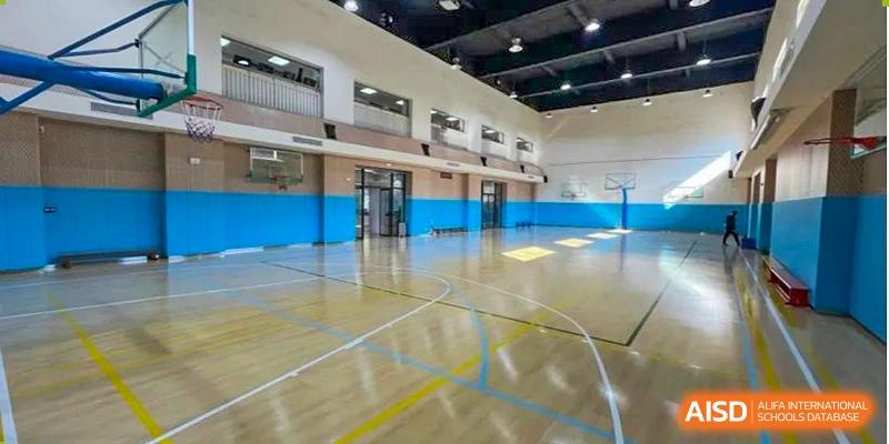 The empty, well-maintained indoor sports hall or gymnasium at The British School of Guangzhou, featuring a wooden floor with court markings.