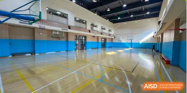 The empty, well-maintained indoor sports hall or gymnasium at The British School of Guangzhou, featuring a wooden floor with court markings.