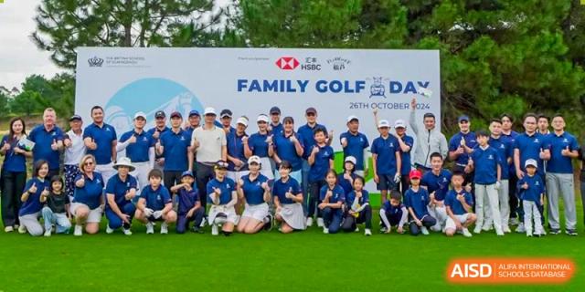 A large group of students and parents from The British School of Guangzhou posing in front of a banner at a Family Golf Day event.