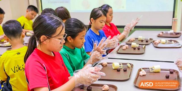Students from The British School of Guangzhou wearing gloves and participating in a baking or cooking class, making pastries or food items.