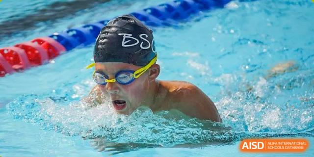A student from The British School of Guangzhou doing a competitive freestyle stroke in the pool, with water splashing around them.