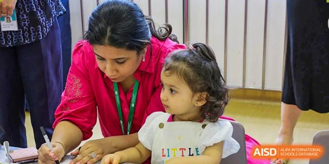 An adult from The British School of Guangzhou staff interacting warmly with a toddler or young child during a school activity or event.
