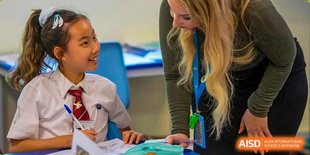 A female teacher from The British School of Nanjing guiding a student during a hands-on learning activity.