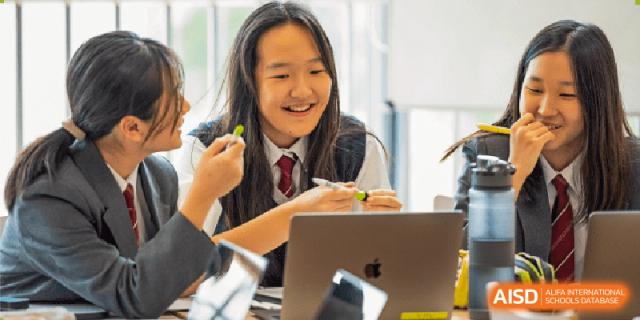 A female student from The British School of Nanjing smiling while working on a laptop.