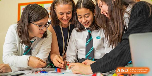 A female teacher from The British School of Nanjing helping students with a science project involving batteries and wires.